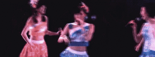 three women are standing next to each other on a stage singing into microphones .