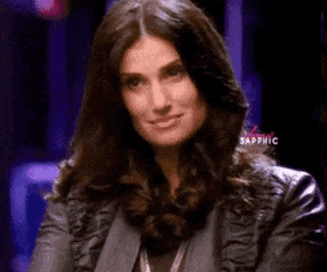 a woman wearing a leather jacket is sitting in front of a purple background with the word sapphic on it