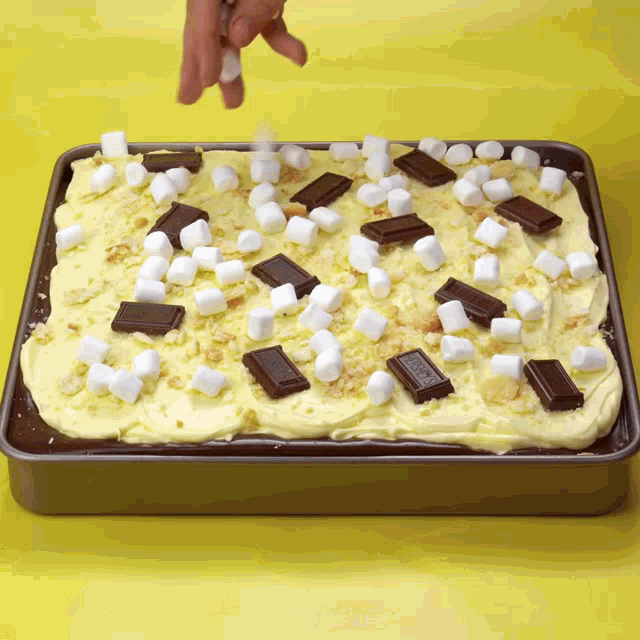 a person is sprinkling marshmallows on top of a cake with a hershey bar