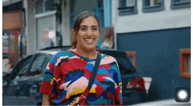 a woman in a colorful shirt is smiling in front of a blue building