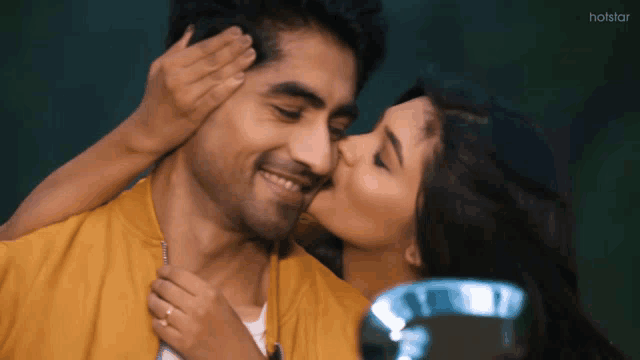 a woman kisses a man on the cheek with a hotstar logo in the corner