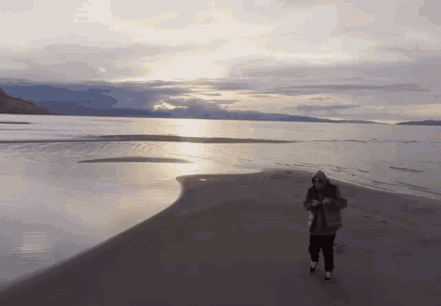 a person in a hooded jacket is walking on the beach