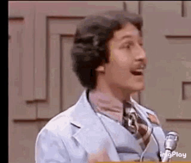 a man in a suit and tie is standing in front of a microphone and talking into it .
