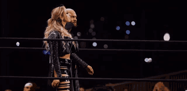 a man and a woman are standing in a wrestling ring at night .