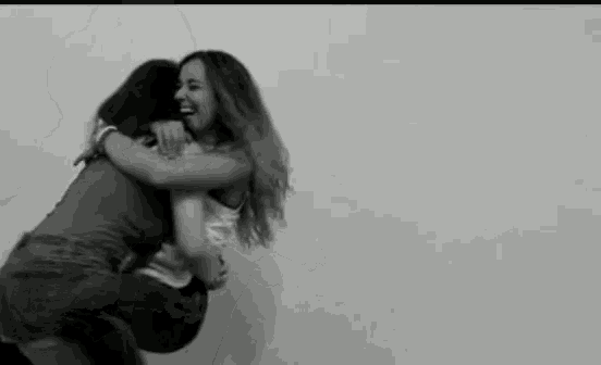 two women are hugging each other in front of a white wall .