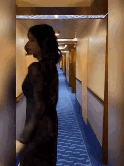 a woman in a black dress is walking down a hallway with a blue carpet