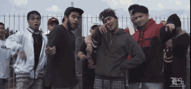 a group of young men standing in front of a fence with the number 2 on their hoodie