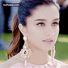 a close up of a woman 's face wearing a pink dress and earrings .