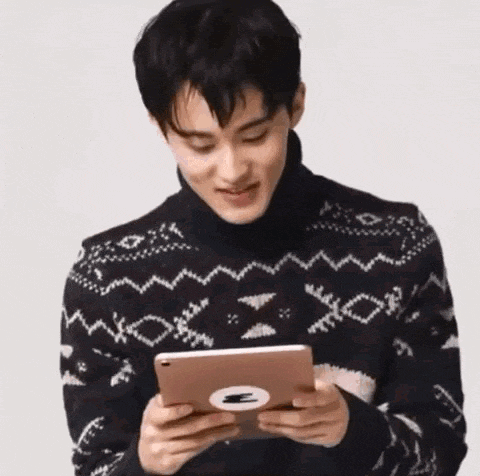 a young man in a sweater is holding a tablet computer .
