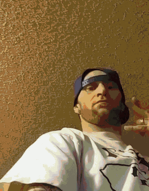 a man with a beard wearing a hat and a white shirt giving the peace sign