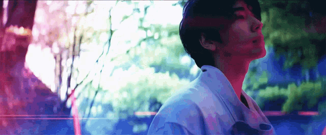 a man in a white shirt is standing in front of a tree in a park .