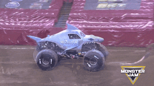 a monster truck with a shark shaped body is driving down a dirt track