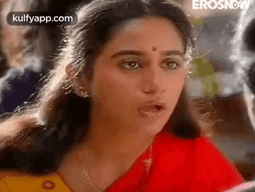 a woman in a red and yellow sari is smoking a cigarette and making a funny face .
