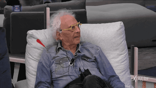 a man wearing glasses sits in a chair with extra hd written on the screen