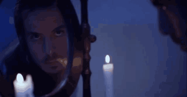 a man in a black jacket stands in front of a sink with candles on it