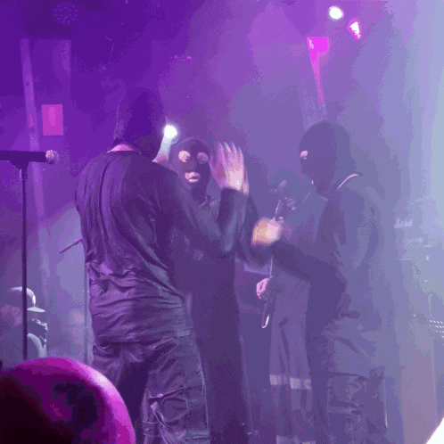 a group of people wearing ski masks on a stage with purple lights