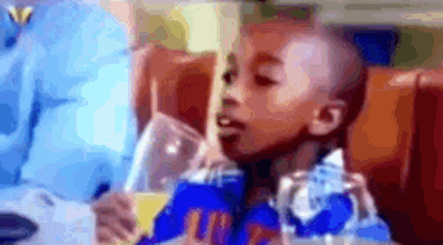 a young boy is sitting at a table drinking from a glass .
