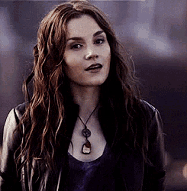 a woman with long hair wearing a leather jacket and a necklace
