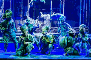a group of people are dancing on a stage in front of a blue background