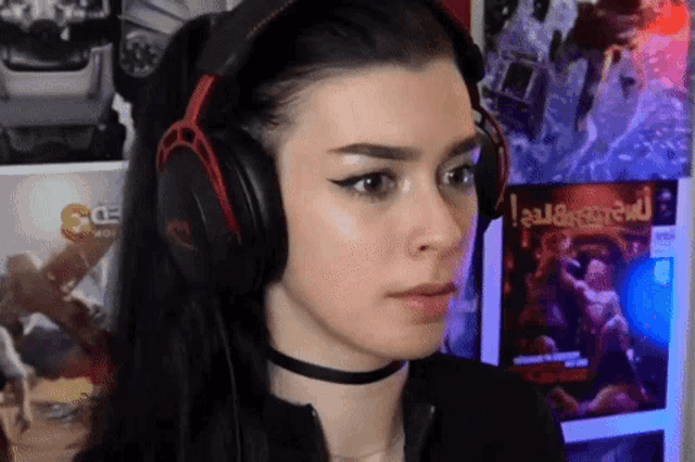a woman wearing headphones and a choker looks at the camera while playing a video game