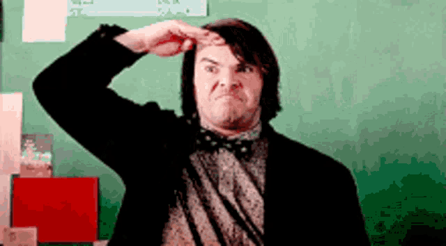 a man in a suit and bow tie is saluting in front of a chalkboard