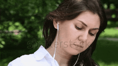 a woman is listening to music with ear buds in a park .