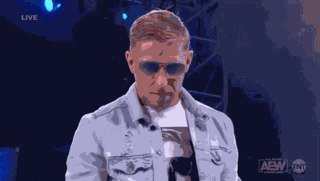 a man adjusts his sunglasses in front of a live audience