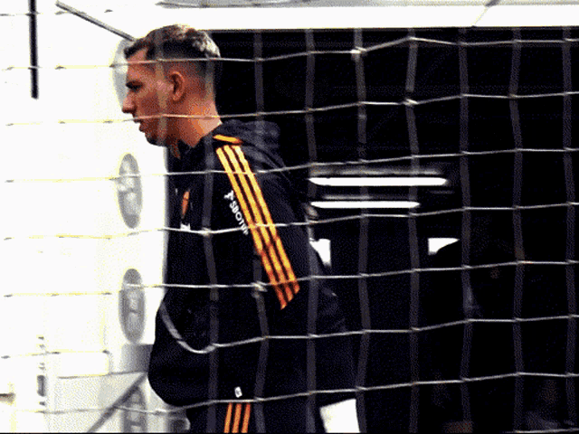 a man behind a fence wearing a jacket that says ' adidas ' on the side