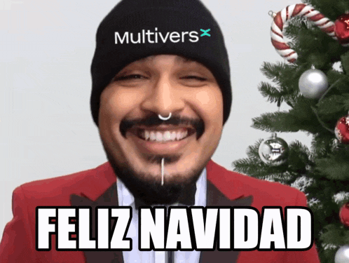 a man wearing a beanie that says multivers x is smiling in front of a christmas tree
