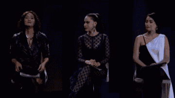 three women are sitting next to each other on a stage in front of a black background .