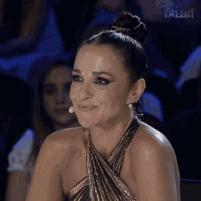 a woman in a gold dress smiles in front of a microphone with the word talent on the bottom