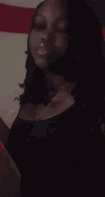 a woman wearing a black top and a necklace is standing in a dark room .