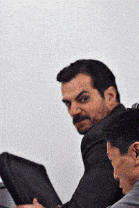a man with a mustache is sitting next to another man with a laptop