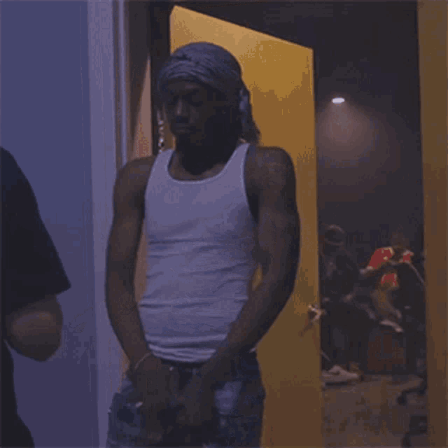 a man in a white tank top is standing in a doorway