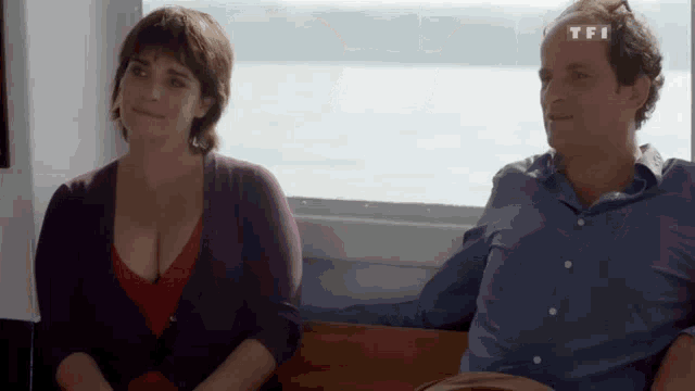 a man and a woman are sitting in front of a window with tfi written on the top of the man 's head