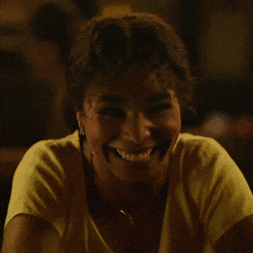 a woman wearing a yellow shirt and necklace smiles