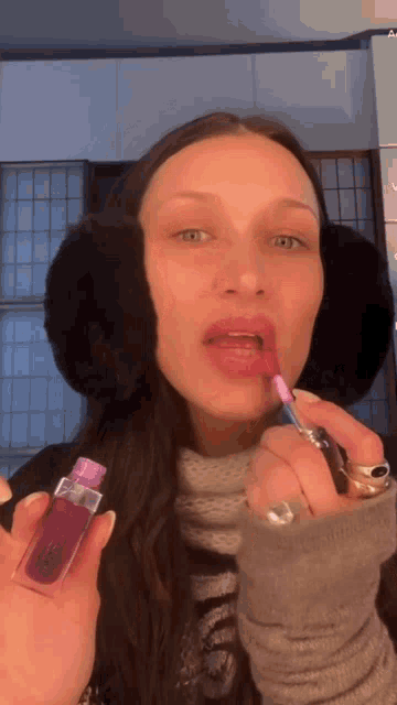 a woman wearing ear muffs is applying pink lipstick