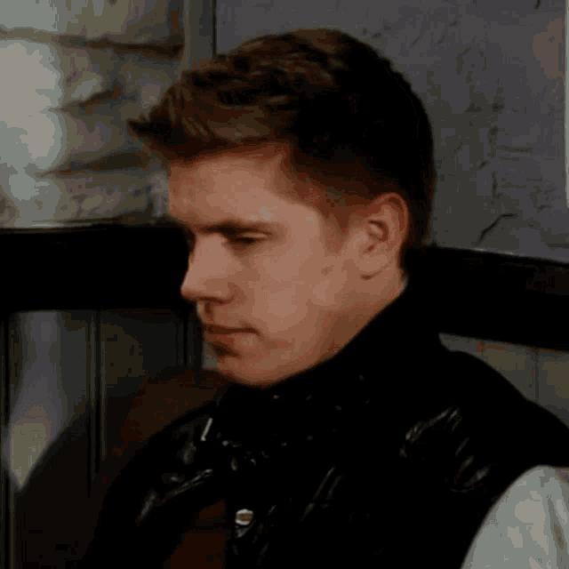 a young man wearing a black leather jacket is making a face