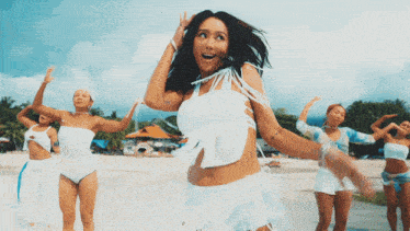 a group of women are dancing on the beach and one has a tattoo on her arm
