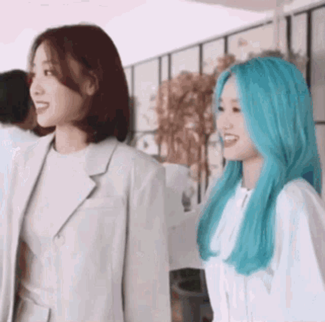 two young women with blue hair are standing next to each other and smiling .