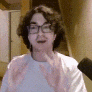 a man with curly hair wearing glasses and ear buds is talking into a microphone .
