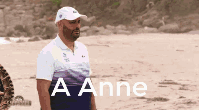 a man wearing a white hat and a blue shirt stands on a beach with the words a anne above him