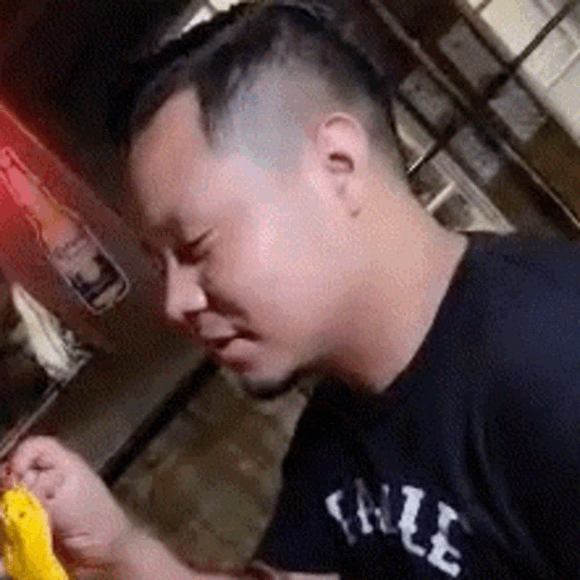 a man in a black t-shirt is eating a hamburger .