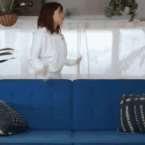 a woman stands in front of a blue couch holding a white curtain