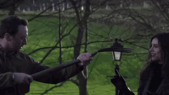 a man is holding a large fork in front of a woman in a park