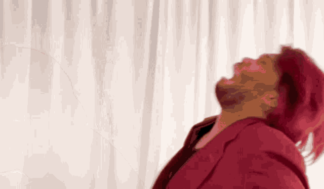 a man with red hair and a beard is standing in front of a white curtain and laughing .