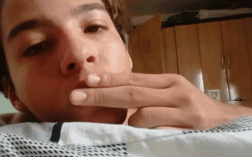 a young man with a tattoo on his forehead is laying on a bed with his hand to his mouth