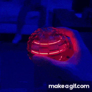 a person is holding a colorful flying ball in their hand in a dark room .