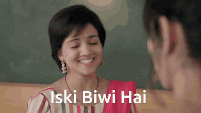 a woman is smiling in front of a blackboard with the words " iski biwi hai " on it