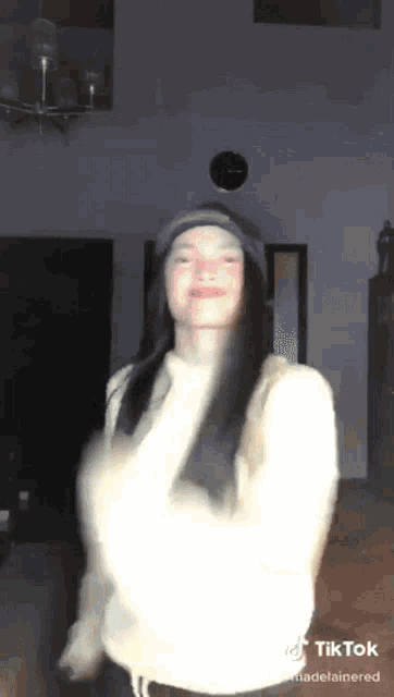 a woman wearing a hat and a white sweater is dancing in a living room .